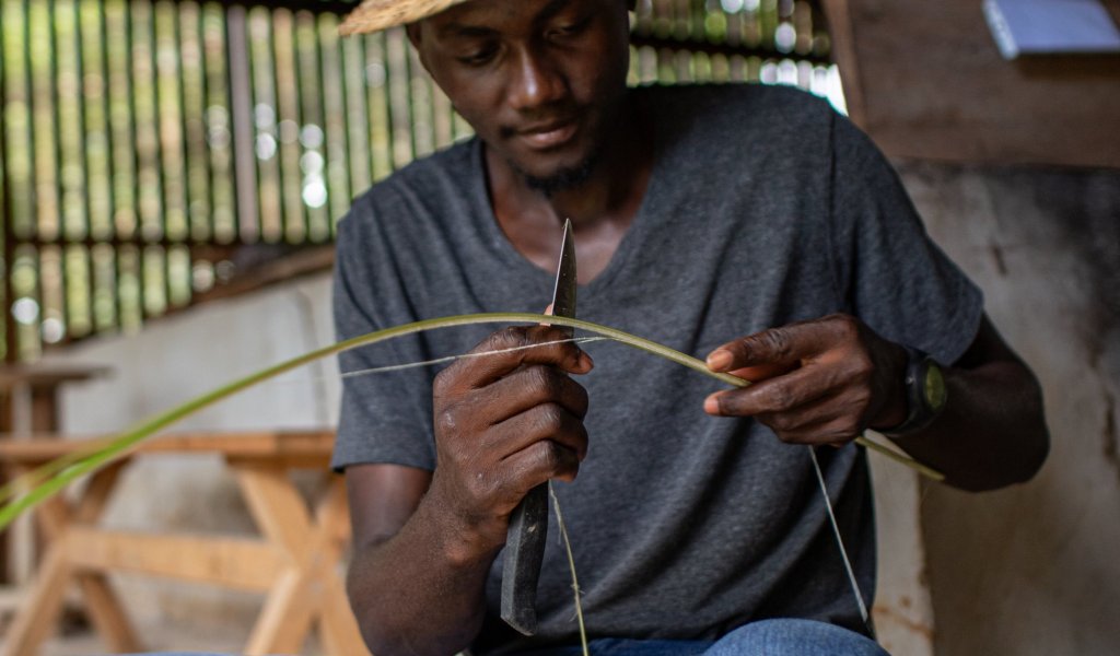 Local man in a hat and jeans weaving baskets on Príncipe Island.