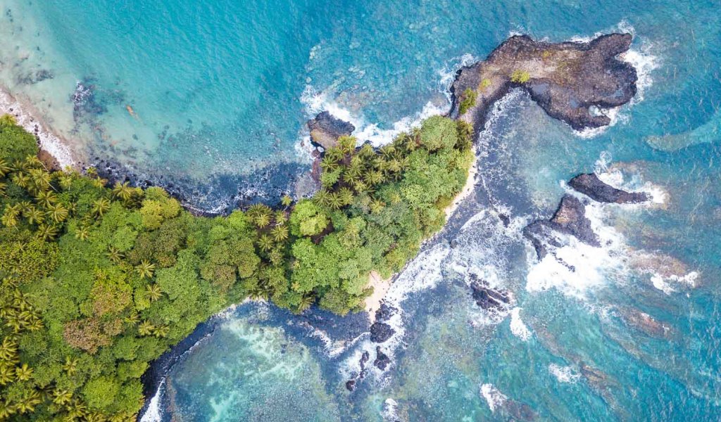 Aerial view of Príncipe Island with crystal-clear turquoise water and lush rainforest vegetation.