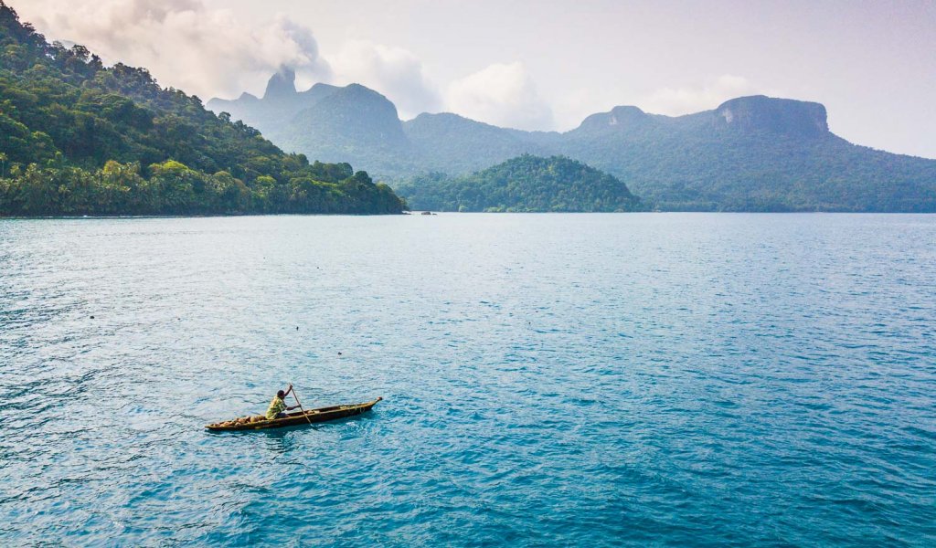 Uma pessoa a flutuar num pequeno barco de madeira sobre o mar perto da Ilha de São Tomé