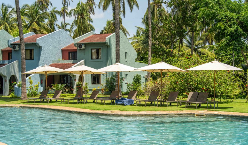 Sun loungers and parasols by the pool at Omali, with pastel-coloured buildings and palm trees in the background, São Tomé Island