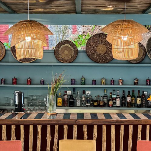 Bar area at Bom Bom Beach Resort with woven lamps and shelves stocked with bottles.