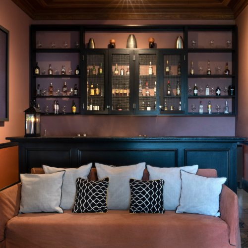 Cozy bar at Roça Sundy with a sofa, cushions, and a display of bottles and glassware