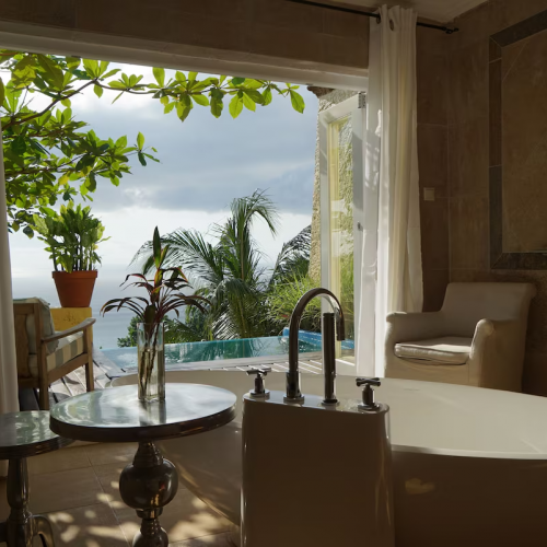 Panoramic Suite bathroom at Belo Monte with freestanding tub, doors to terrace and plunge pool, ocean view through tropical leaves.