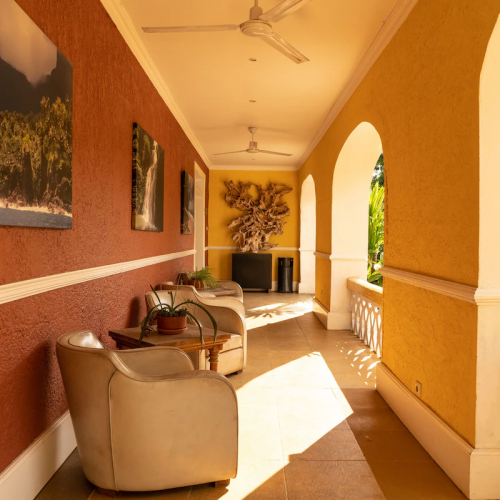 Sunny arcade porch at Belo Monte with arches, armchairs and wall art, looking onto tropical plants.