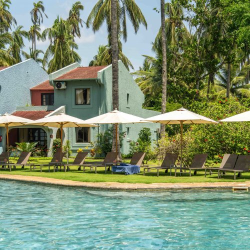 Sun loungers and parasols by the pool at Omali, with pastel-coloured buildings and palm trees in the background, São Tomé Island