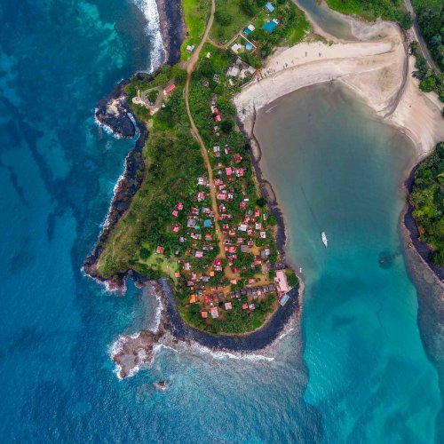 Top-down aerial view of the village of Água Izé on a peninsula surrounded by turquoise waters, São Tomé Island