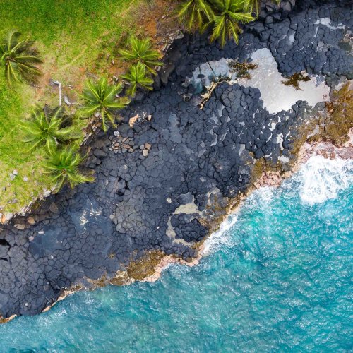 Aerial view of dark volcanic rocks meeting the turquoise ocean at Boca do Inferno, São Tomé Island