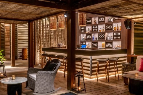 A drinks bar with bottles on shelves, davor sitzgelegenheiten at Sundy Praia