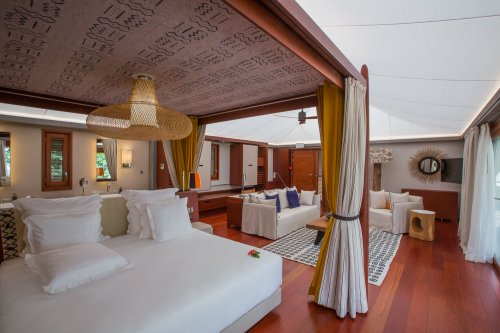 Quarto com cama de casal elegante, tapete artístico, área de estar e mesa ao fundo no Sundy Praia.