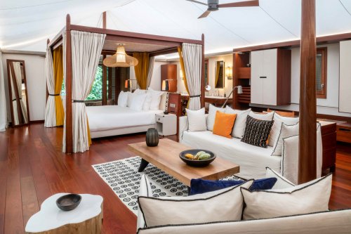 Quarto com cama de dossel elegante, tapete artístico, área de estar e mesa de madeira em primeiro plano na tenda-vila Sundy Praia.