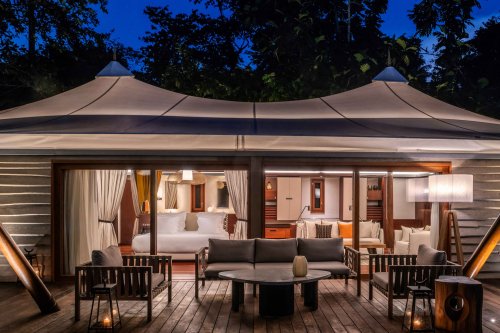 Exterior view of the tent villa at Sundy Praia by night, with the illuminated bedroom in the background and the terrace in the foreground.