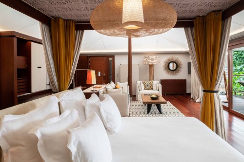 Quarto com cama de casal elegante, tapete artístico, área de estar e mesa ao fundo no Sundy Praia.