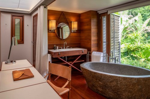 Table in the foreground, large high-quality granite bathtub, with a view through the window of the lush rainforest vegetation.