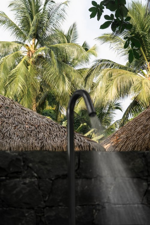 Outdoor shower with thatched roofs and palm trees at Bom Bom Beach Club