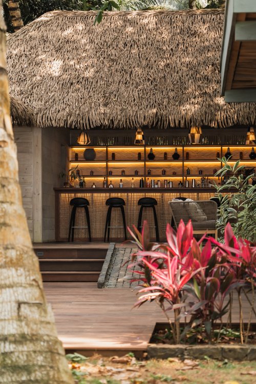 Bar com cobertura de colmo, bancos altos e prateleiras retroiluminadas no Bom Bom Beach Club