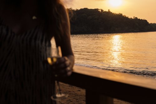 Um homem segurando uma bebida na praia durante o pôr do sol no Bom Bom Beach Resort.