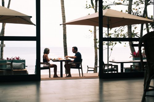 Two people sitting at an outdoor restaurant at Bom Bom Beach Resort with a hazy background.