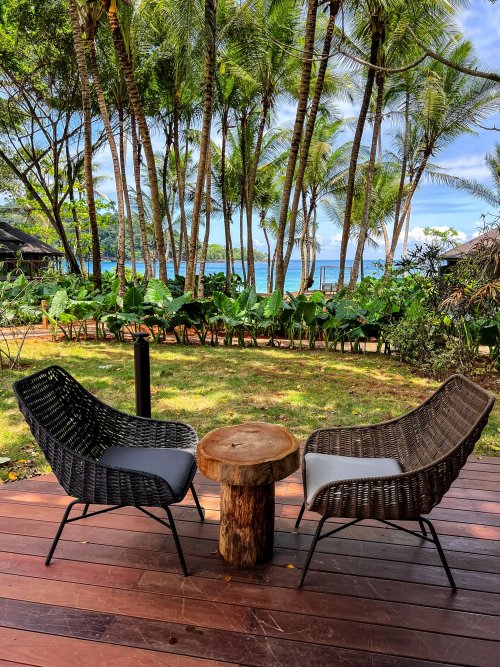 Duas cadeiras e uma mesa em uma varanda com vegetação exuberante ao fundo no Bom Bom Resort.