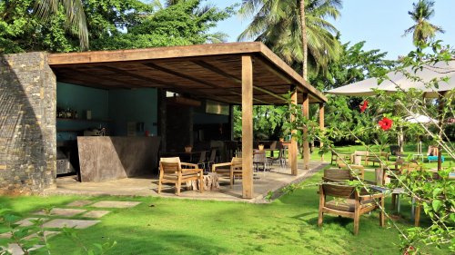 Área externa do bar e restaurante com cadeiras de madeira e vegetação exuberante no Omali Hotel, São Tomé