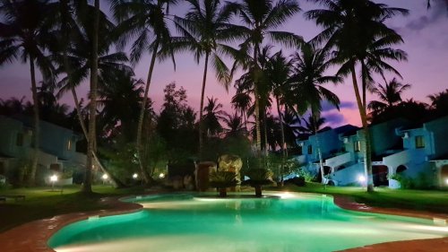 Piscina à noite no Omali, iluminada com luz suave em meio à vegetação exuberante.