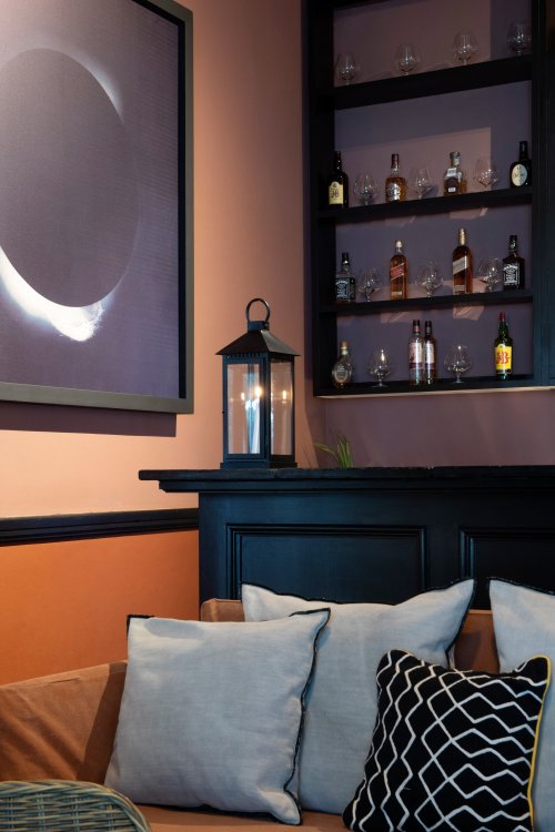 Cozy bar at Roça Sundy with a sofa, cushions, and a display of bottles and glassware