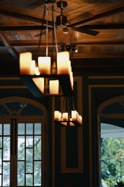 Lustre suspenso com velas, teto de madeira e janela ao fundo na Roça Sundy