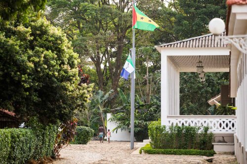 Exterior view of Roça Sundy entrance with white pillars, arched windows, and lush greenery