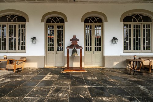 Entrance of Roça Sundy with colonial-style doors, a bell, and wooden chairs on the porch