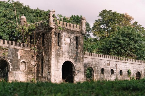 Ruínas de um antigo edifício de pedra rodeado por vegetação exuberante