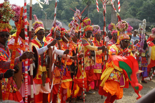 Desfile carnavalesco no Príncipe, figurantes em trajes tradicionais coloridos com bandeiras, varas e tambores.