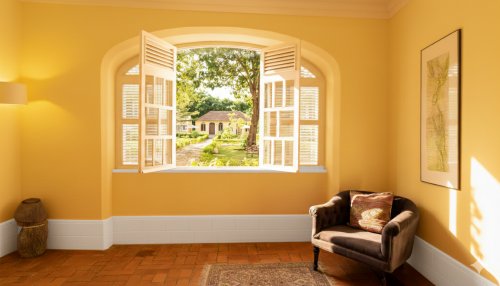 Sunlit window at Belo Monte opening to the courtyard gardens with yellow buildings and a cosy armchair inside.