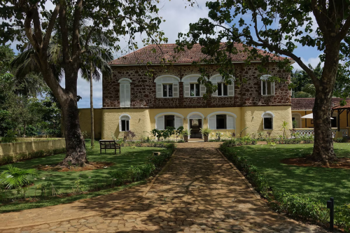 Main house of Belo Monte framed by trees, stone and yellow facade with arched windows and garden walkway.