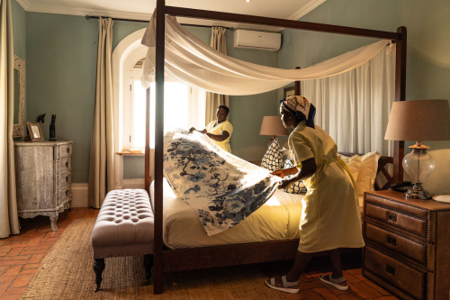 Housekeeping preparing a four-poster bed with floral cover in the Panoramic Suite at Belo Monte, soft morning light.