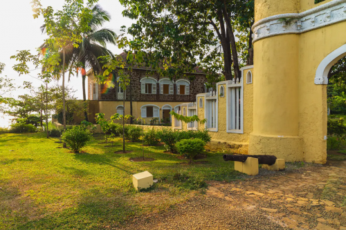 Main house of Belo Monte framed by trees, stone and yellow facade with arched windows and garden walkway.
