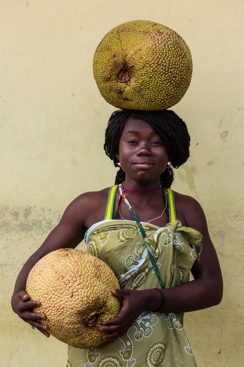 Retrato de uma mulher sorridente a equilibrar uma grande fruta na cabeça