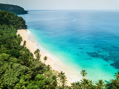 Areal view of a tropical empty beach with turquoise water and lush jungle behind
