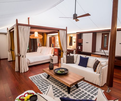 Bedroom with elegant four-poster bed, artistic rug, seating area, and wooden table in the foreground at Sundy Praia tent villa.