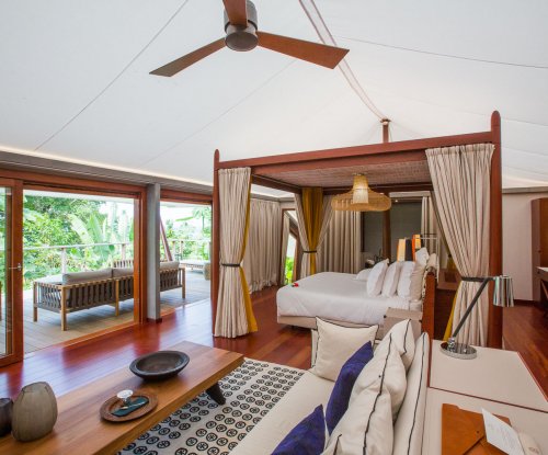 Bedroom with elegant four-poster bed, artistic rug, seating area, and wooden table in the foreground at Sundy Praia tent villa.