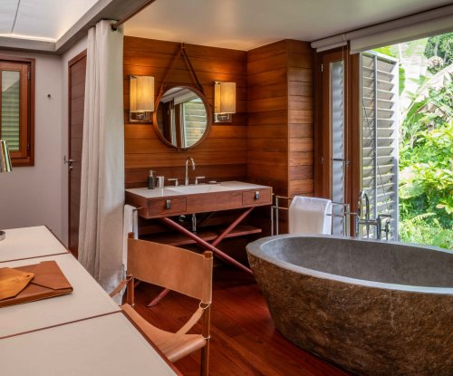 Mesa em primeiro plano, grande banheira de granito de alta qualidade, com vista através da janela para a vegetação exuberante da selva.