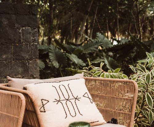 Rattan lounge chair with patterned cushion and green glass on a wooden table at Bom Bom Beach Club