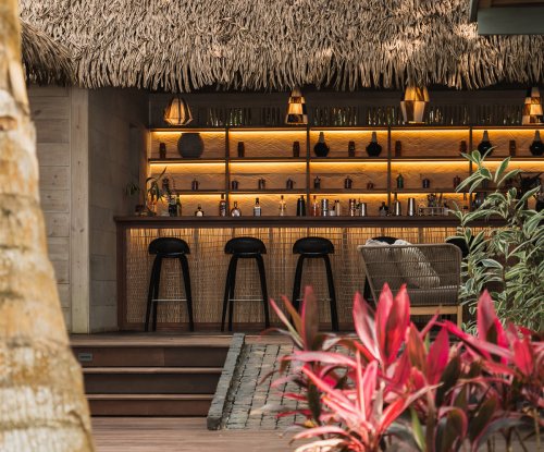 Thatched-roof bar with high stools and backlit shelves at Bom Bom Beach Club