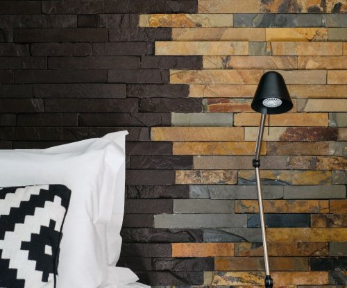 Cama com almofada estampada e parede de pedra ao fundo