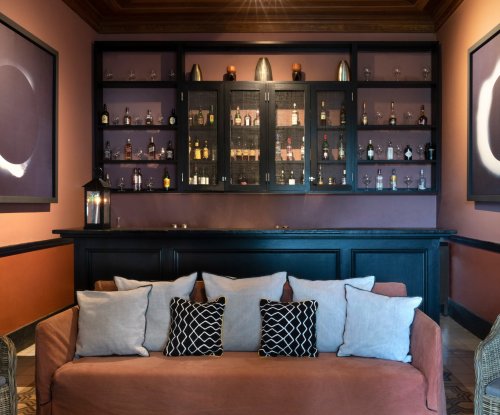 Cozy bar at Roça Sundy with a sofa, cushions, and a display of bottles and glassware