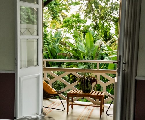 View from a bedroom at Roça Sundy showing a balcony with a chair, table, and lush greenery