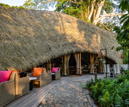 Vista exterior do restaurante OKA Sundy com teto de palha, área de estar ao ar livre e vegetação densa