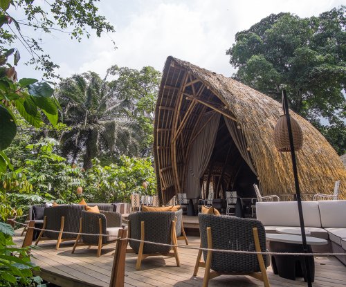 Área de estar ao ar livre e estrutura de bambu do restaurante OKA Sundy rodeada por vegetação densa