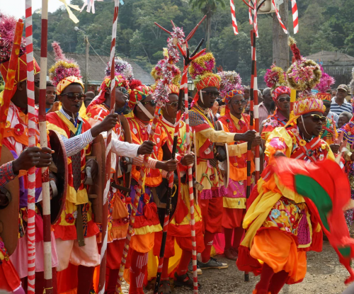 Carnival parade on Príncipe, performers in bright traditional costumes with flags, sticks and drums.