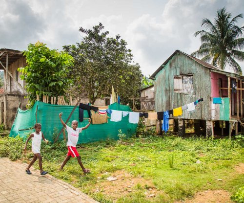 Duas crianças a rir para a câmara, com cabanas locais e roupa estendida a secar ao fundo.