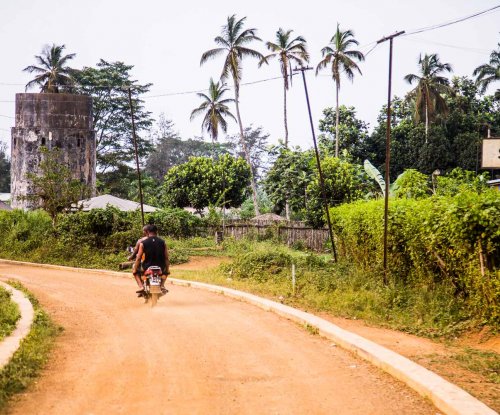 Two locals riding a motorbike on a dirt road in Sundy, Príncipe Island.