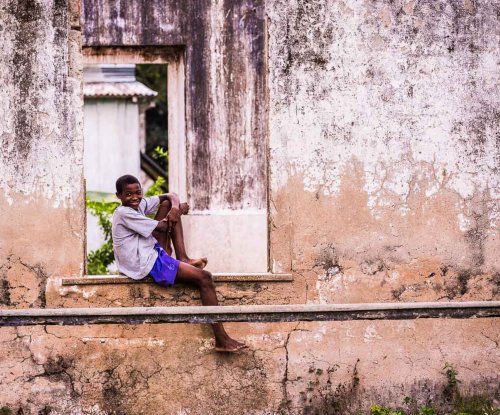 Criança com calções roxos e uma T-shirt magenta sentada num banco de janela ao ar livre